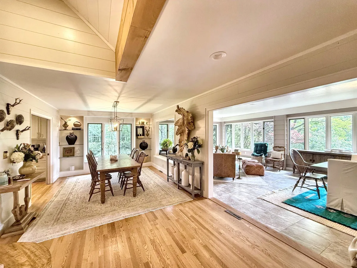 A spacious dining area featuring a large table, abundant natural light streaming through large windows, decorative wall art, and greenery in vases. The atmosphere is set for both warm family dinners and festive gatherings.