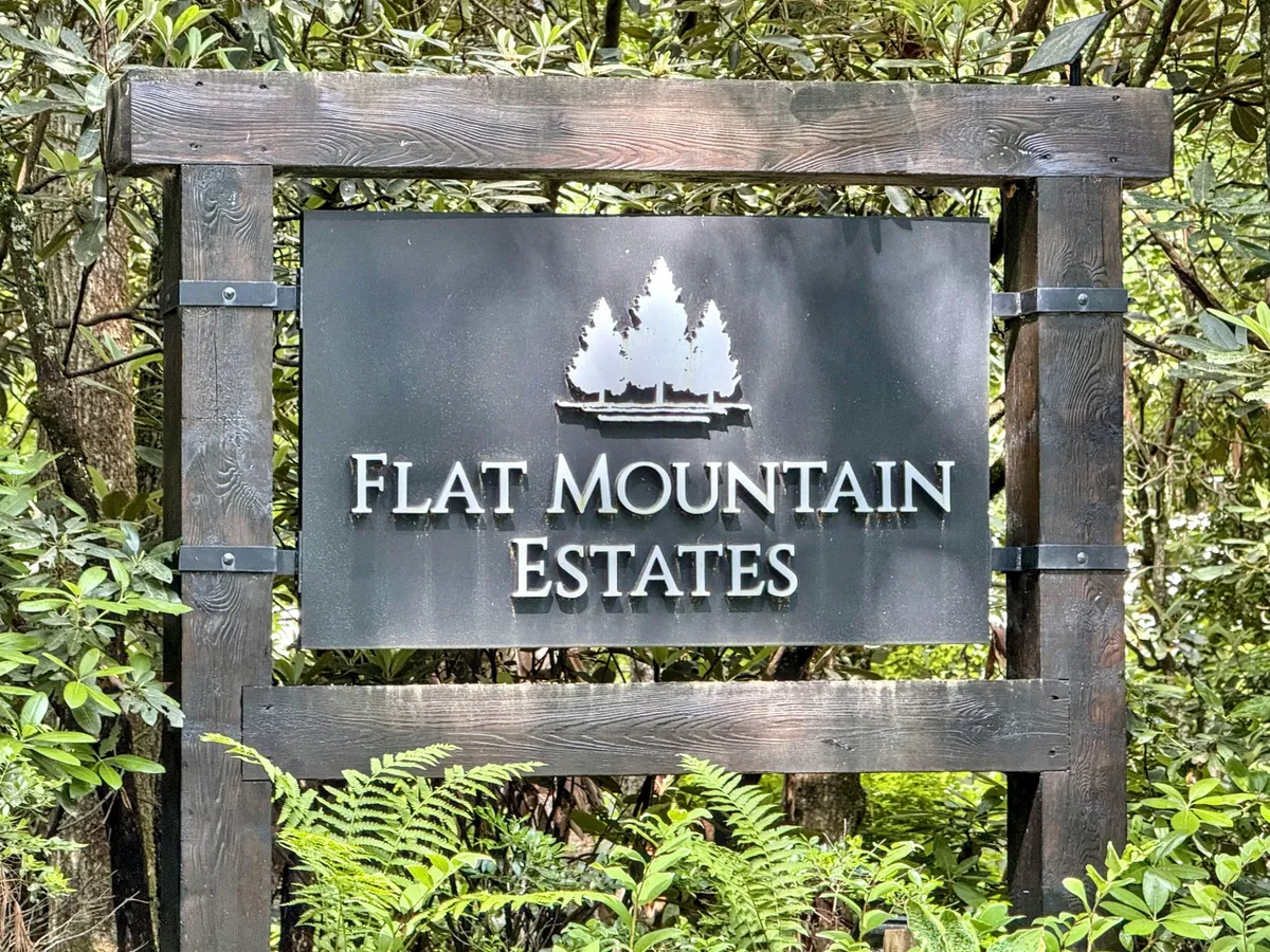 The Flat Mountain Estates sign is surrounded by verdant greenery, setting the tone for an exclusive, nature-filled community. The image evokes the tranquility and accessibility of local trails and outdoor amenities, reinforcing the sense of adventure just steps from your door.