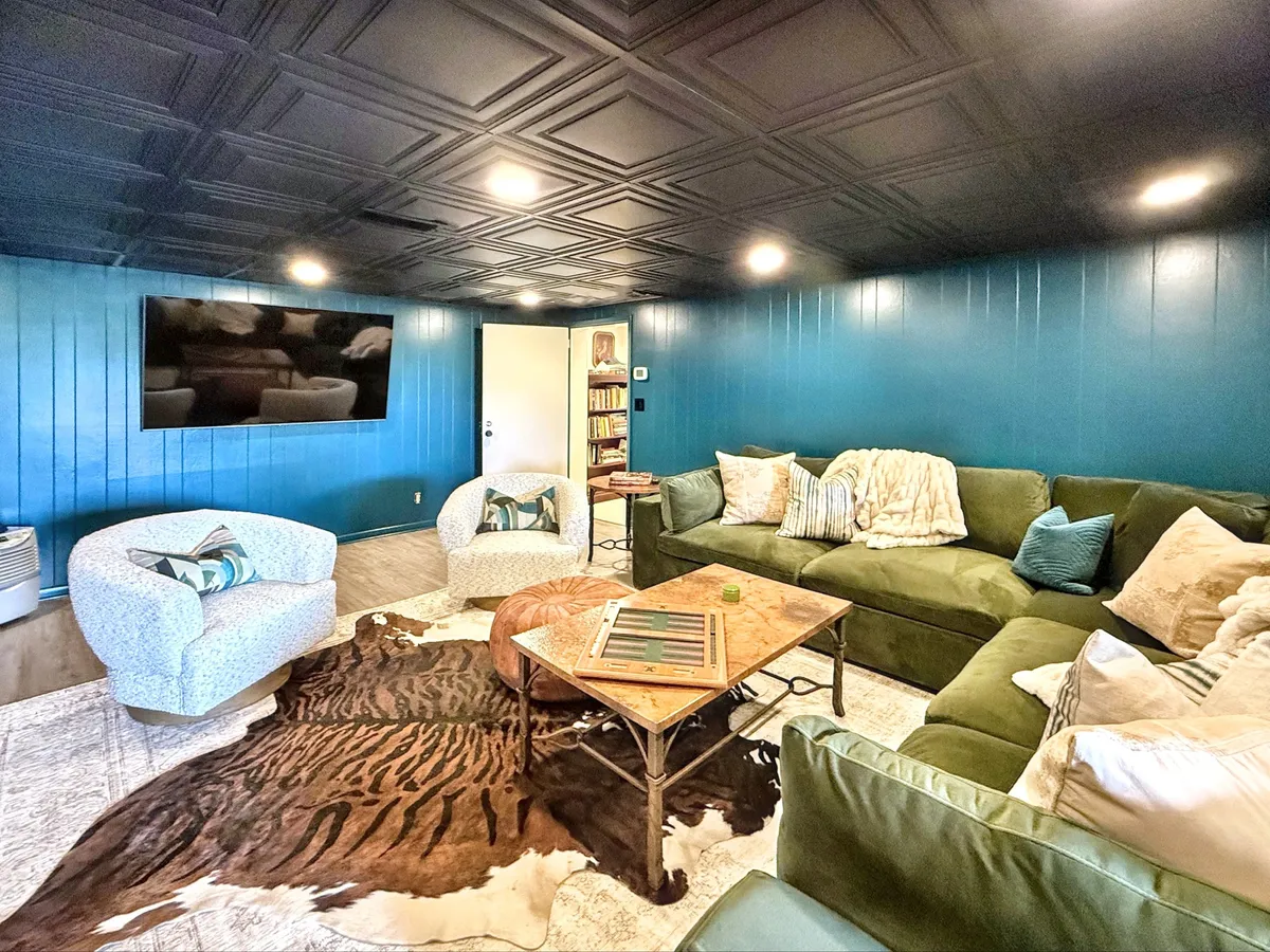This image features a large green sectional sofa and blue accent chairs arranged around a coffee table, with a TV on the wall and a cowhide rug anchoring the space. The inviting layout and plush seating create a perfect environment for group entertainment and movie marathons.