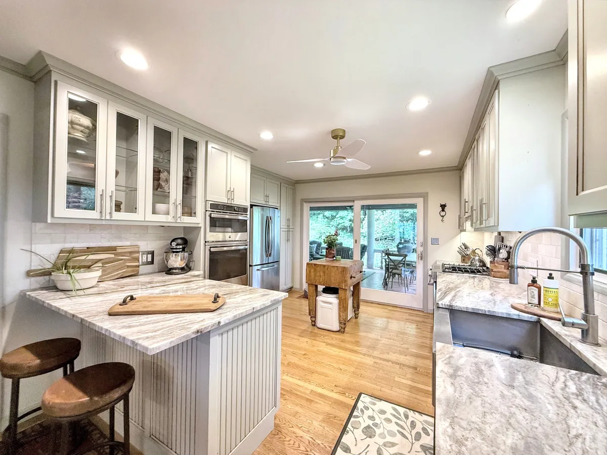 A spacious, fully equipped kitchen with a large island, stainless steel appliances, and expansive windows that overlook the outdoor area. Warm wooden accents and inviting lighting create a welcoming atmosphere ideal for cooking and social gatherings.
