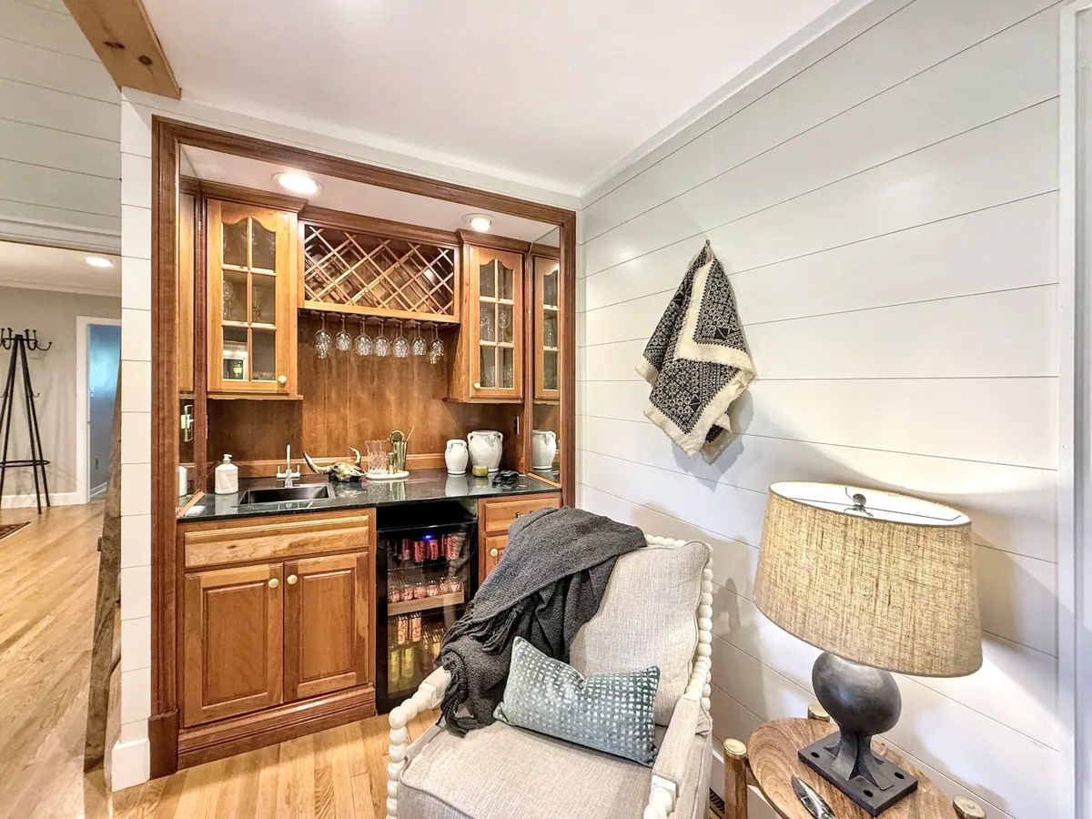 A cozy bar area with a welcoming atmosphere, featuring a bar counter, a plush chair, and stylish lighting. The setting encourages intimate socializing and relaxing with a drink.