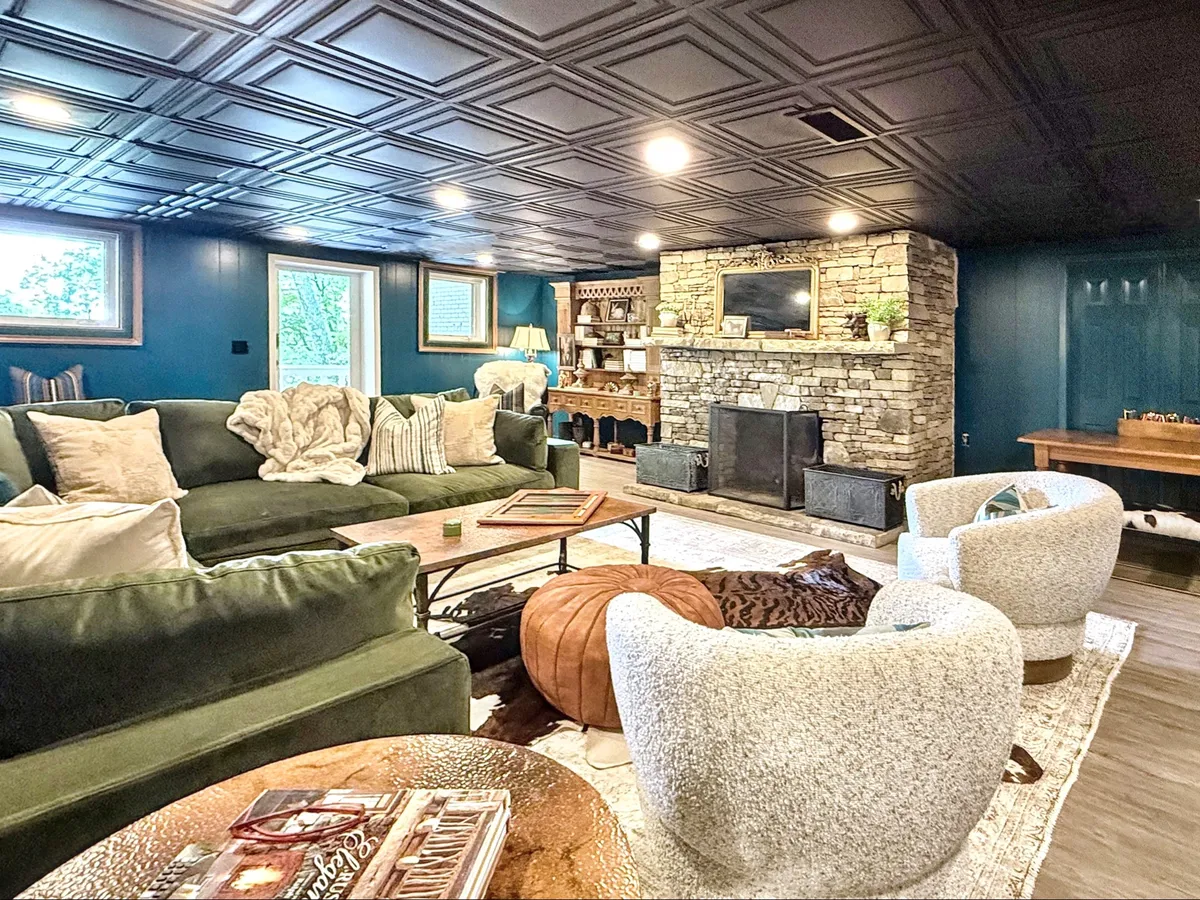 A large living space that blends a green sectional sofa, textured accent chairs, a stone fireplace, and a wooden side table. The setting is designed for group gatherings, with ample seating and a warm, communal ambiance.
