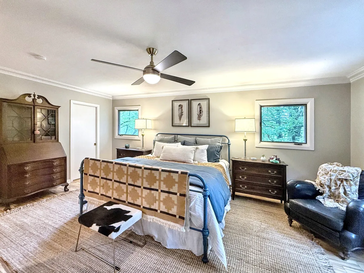 A peaceful bedroom showcasing a bed with a patterned throw, a dark wooden dresser, a comfortable reading chair, and framed artwork on the wall. The space exudes tranquility, perfect for quiet moments of reflection or a restful night.