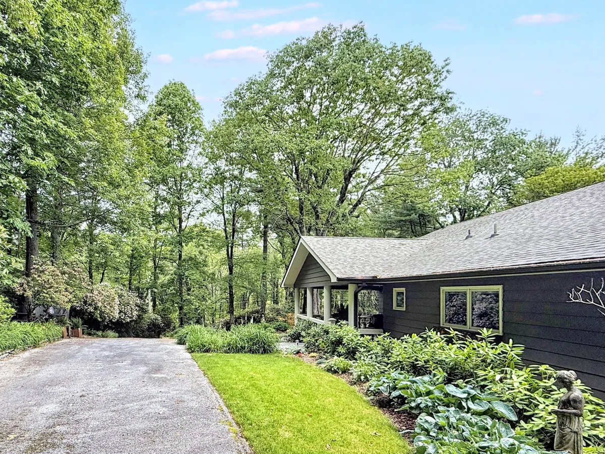 This image shows the exterior of the house, with a welcoming driveway, a well-tended garden, mature trees, and a distinctive statue. The peaceful porch and inviting outdoor areas hint at the comfort and leisure awaiting inside.
