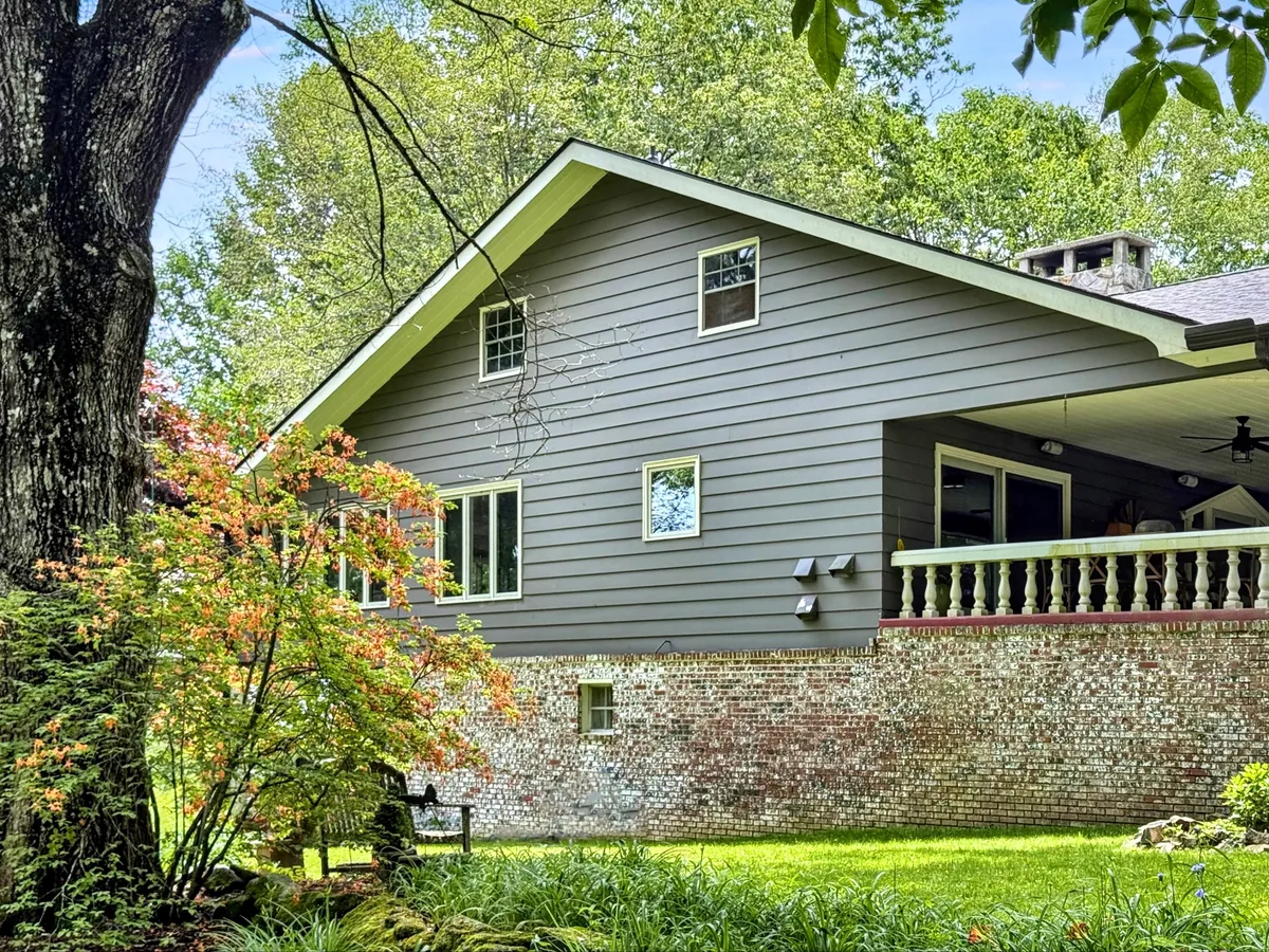This exterior image shows the house against a backdrop of surrounding greenery and flowering plants, with a welcoming brick wall and visible porch area, hinting at the home's harmonious integration with its natural surroundings.