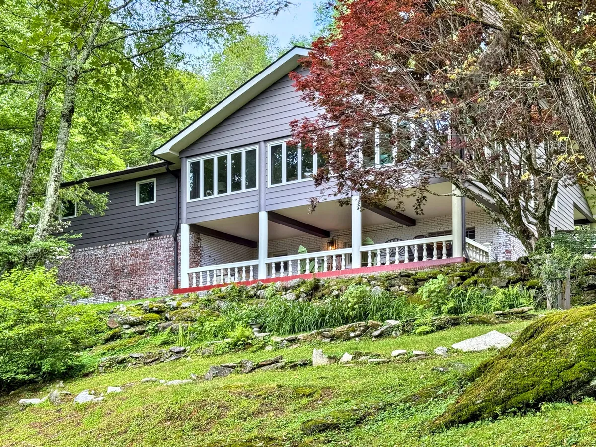 An inviting view of a house with large windows and a decorative porch railing, nestled within abundant greenery. The porch and yard offer beautiful vistas, ideal for yoga, morning coffee, or simply enjoying the mountain views mentioned in the text.